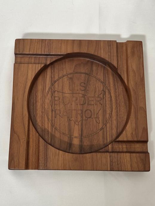 Elevate your cigar experience with this handcrafted Four-Person Solid Walnut Cigar Tray, featuring a stunning epoxy inlay of the US Border Patrol logo. Measuring 12" x 12" and 1.5" thick, this elegant tray is designed to hold up to four cigars, making it perfect for shared moments and celebrations. The rich, natural beauty of solid walnut combined with the precision epoxy inlay creates a luxurious and patriotic centerpiece for any gathering.