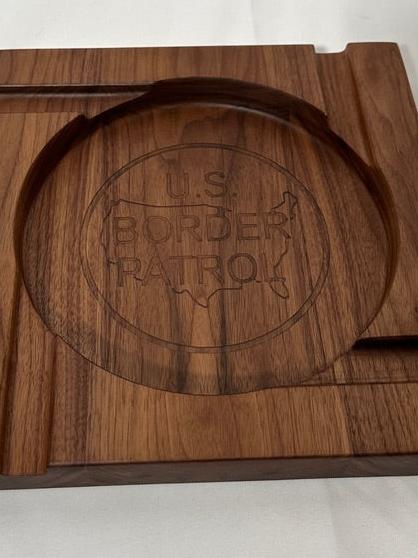 Elevate your cigar experience with this handcrafted Four-Person Solid Walnut Cigar Tray, featuring a stunning epoxy inlay of the US Border Patrol logo. Measuring 12" x 12" and 1.5" thick, this elegant tray is designed to hold up to four cigars, making it perfect for shared moments and celebrations. The rich, natural beauty of solid walnut combined with the precision epoxy inlay creates a luxurious and patriotic centerpiece for any gathering.