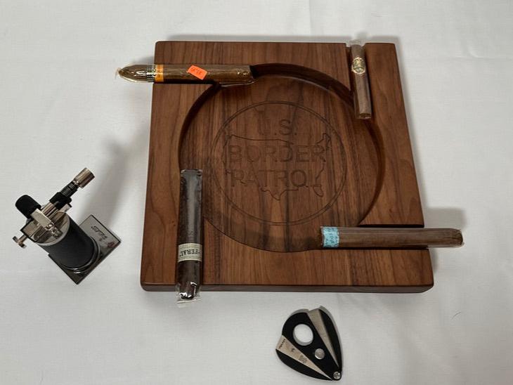 Elevate your cigar experience with this handcrafted Four-Person Solid Walnut Cigar Tray, featuring a stunning epoxy inlay of the US Border Patrol logo. Measuring 12" x 12" and 1.5" thick, this elegant tray is designed to hold up to four cigars, making it perfect for shared moments and celebrations. The rich, natural beauty of solid walnut combined with the precision epoxy inlay creates a luxurious and patriotic centerpiece for any gathering.