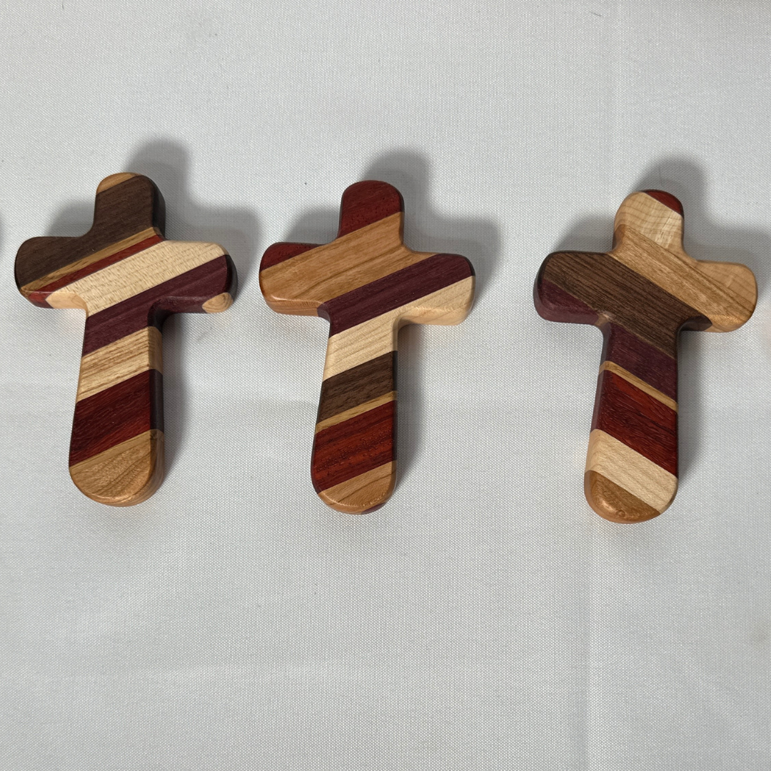 Experience the perfect blend of faith, craftsmanship, and personalization with our Handcrafted Wooden Prayer Cross. Measuring approximately 5" x 3-1/4", this hand-sized cross is thoughtfully designed for prayer, meditation, and comfort. Crafted from premium hardwoods, including purple heart, paduak, hard maple, walnut, white oak, and cherry, each cross showcases a stunning array of natural tones and textures.