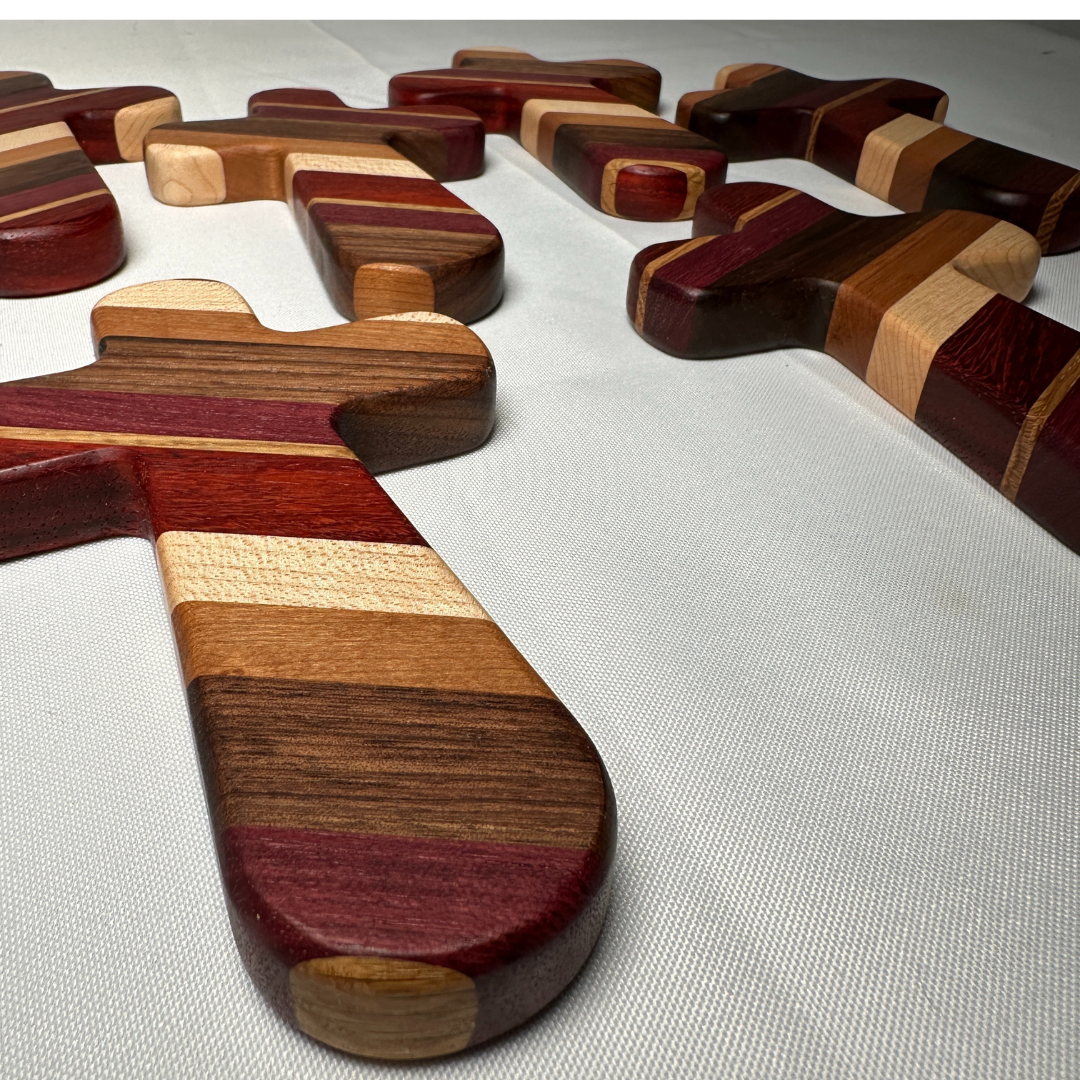 Add a timeless touch of faith and artistry to your home with this handcrafted wooden cross. Measuring 6-1/2" long by 4-1/8" wide, this cross is carefully crafted from premium strips of purple heart, paduak, white oak, hard maple, walnut, and cherry woods. Each cross is a unique piece, showcasing the natural beauty and rich tones of these high-quality hardwoods.